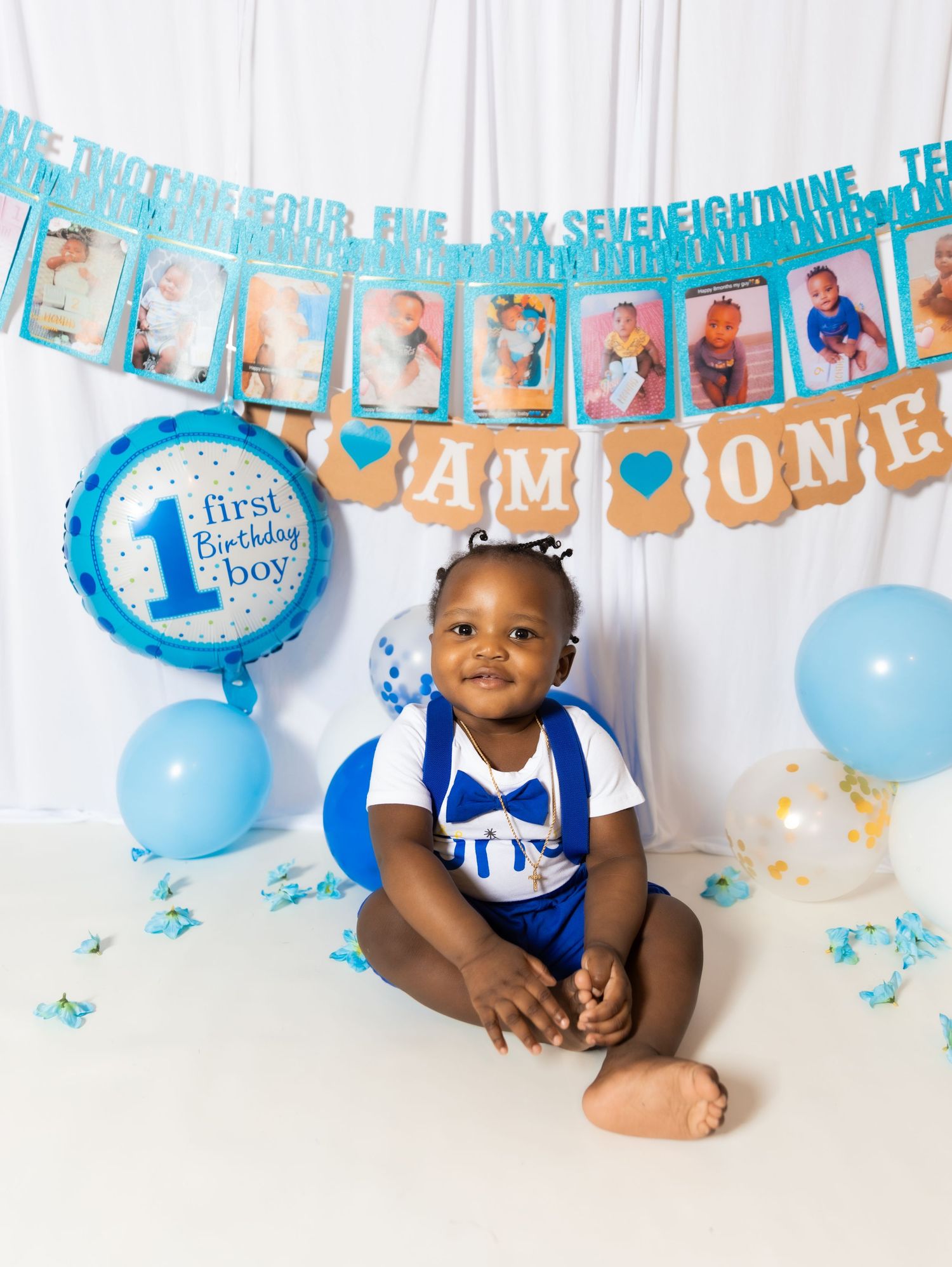 Baby boy sits before a first birthday banner and balloons in blue and gold party decorations.