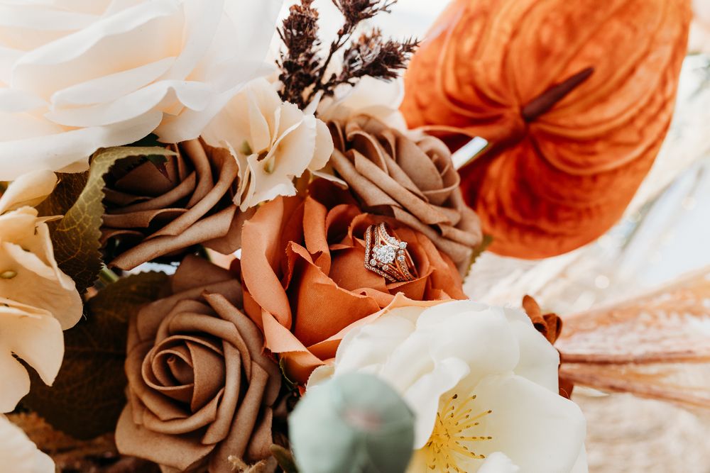 Diamond engagement ring nestled in autumn wedding bouquet with rust and brown roses.