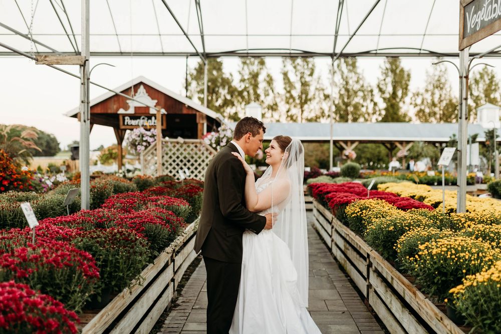 Bride and groom share romantic moment among colorful flowers in greenhouse setting.
