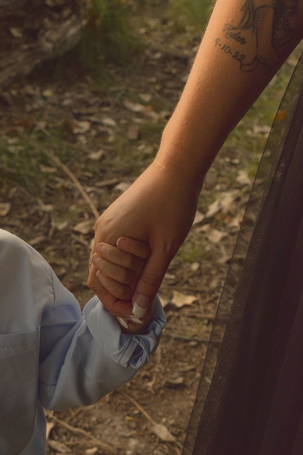 Close-up of hands with tattoos holding a tissue or paper in a natural outdoor setting.