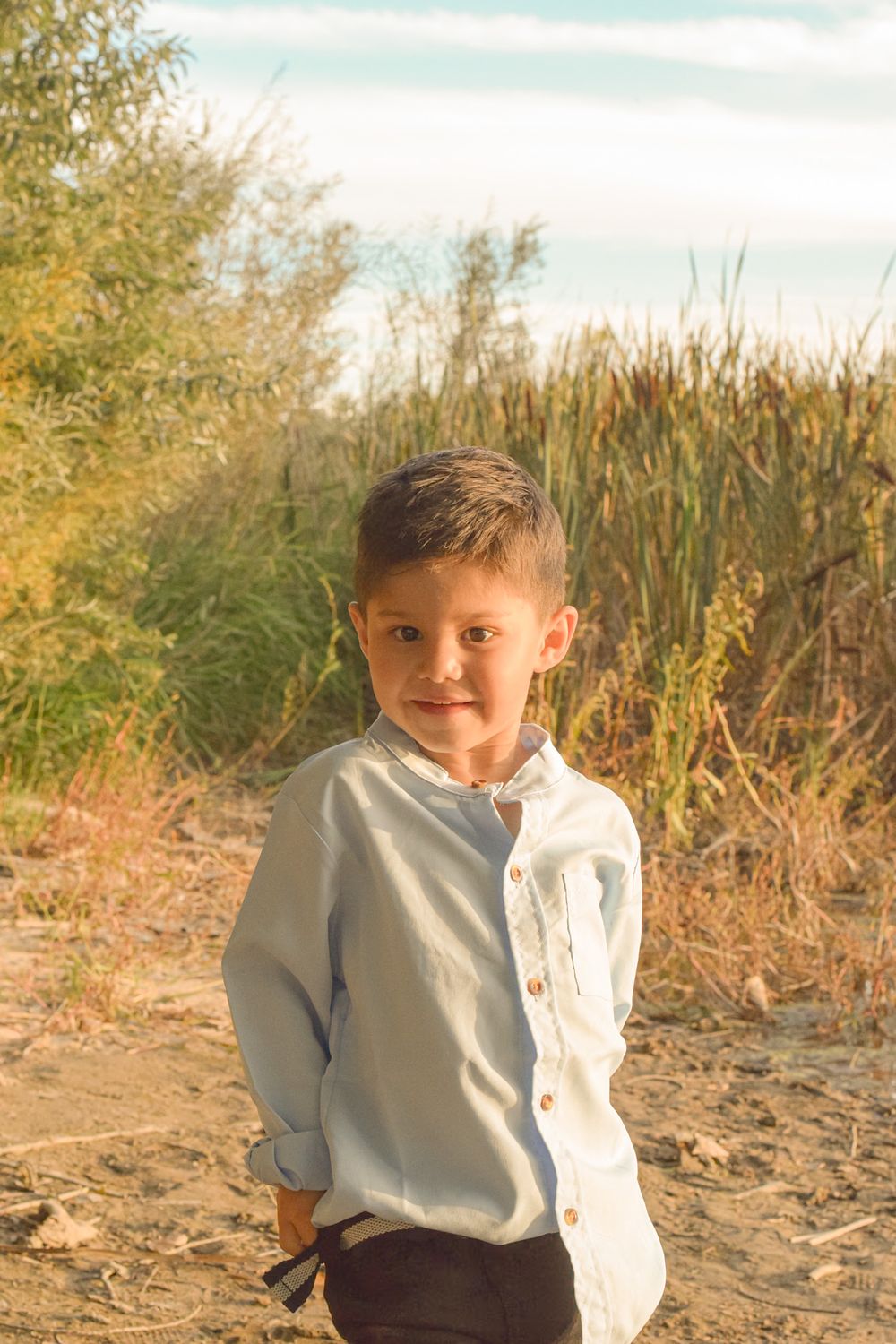 Young child in white shirt sitting on sandy ground during golden hour.