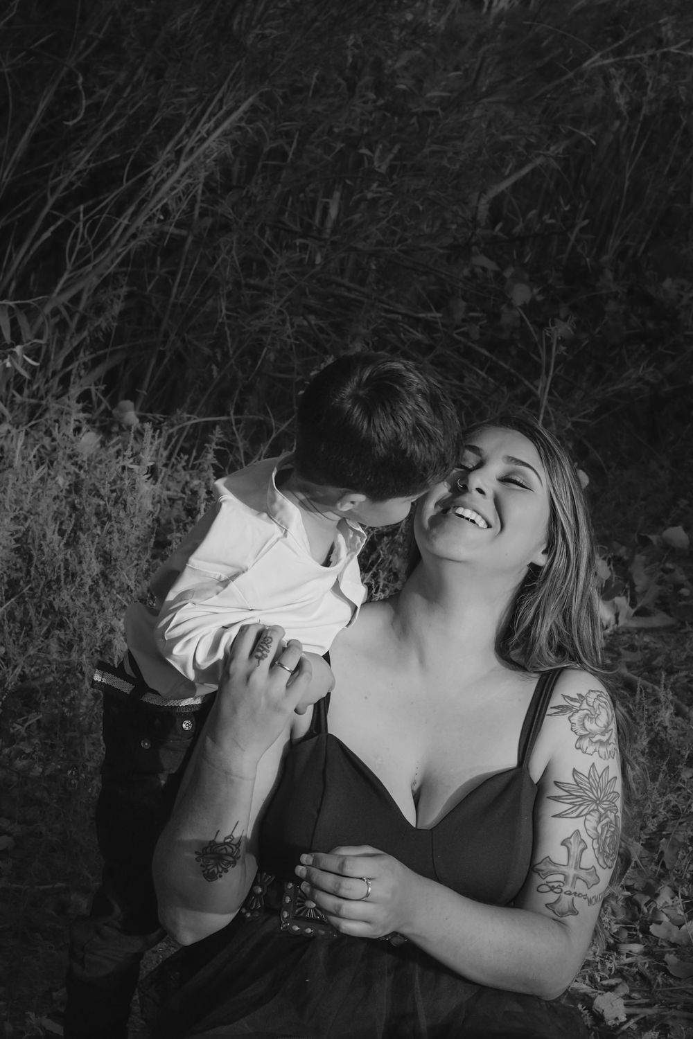 Black and white portrait of a person with tattoos lying down outdoors.