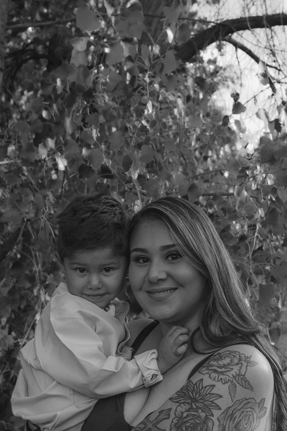 Black and white portrait of two people posing together under tree branches.