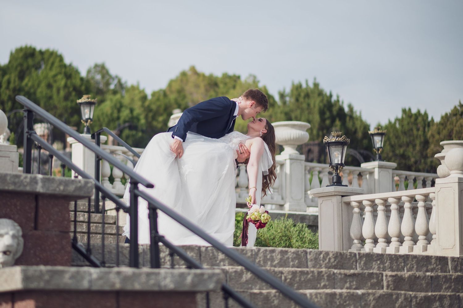 Groom dipping bride at the top of an outdoor garden staircase.