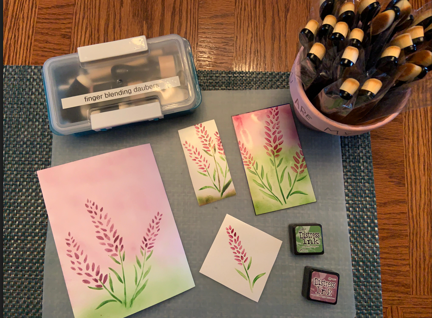 Work space displaying card panels made with the layered lavender stencil, ink pads, and ink blending tools.