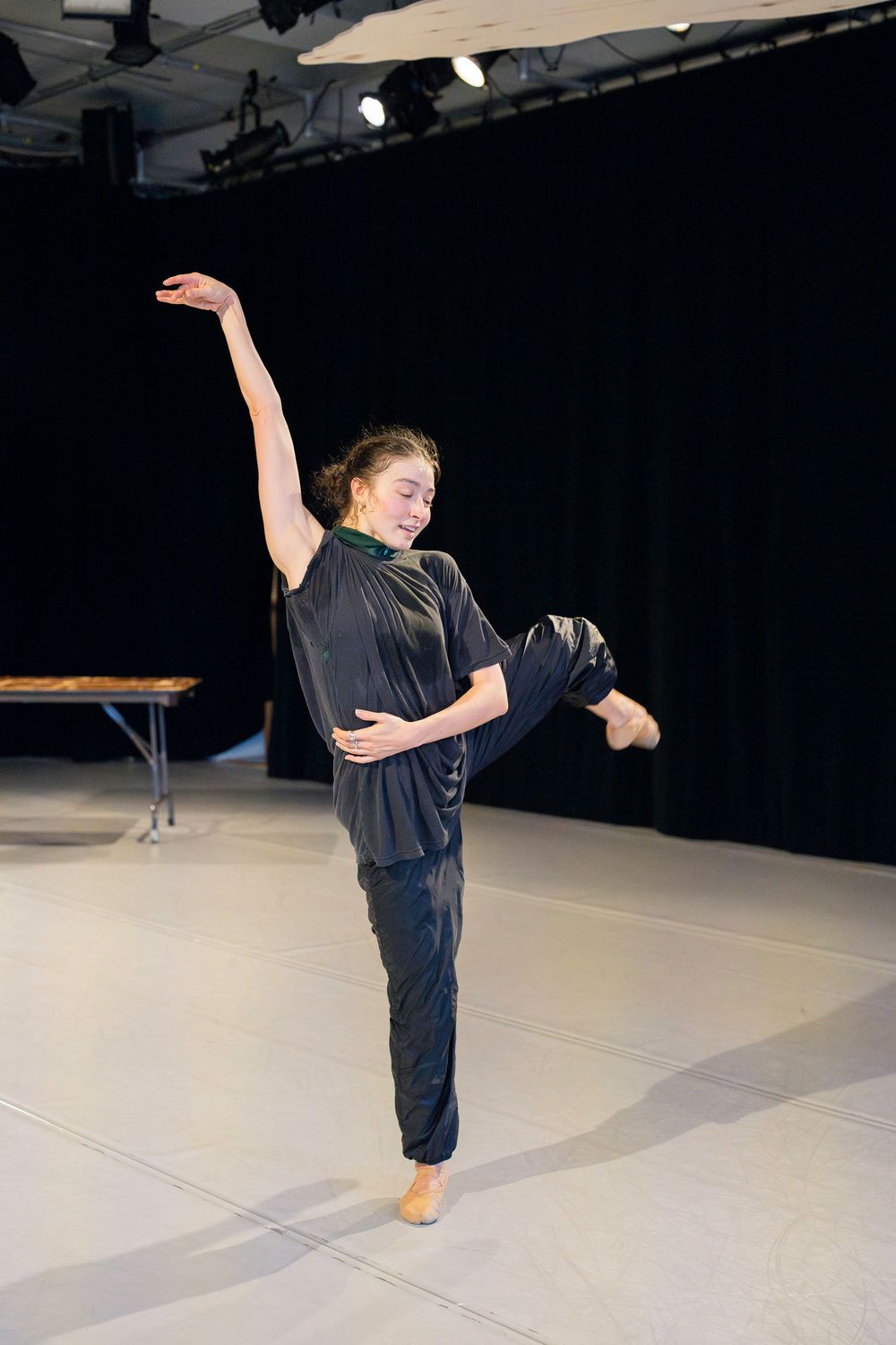 Dancer performs a graceful high kick in a black outfit on stage during a contemporary dance performance.