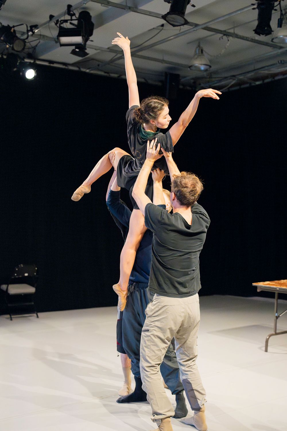 Two dancers perform a contemporary dance piece in a white studio space with dramatic lighting and coordinated movements.