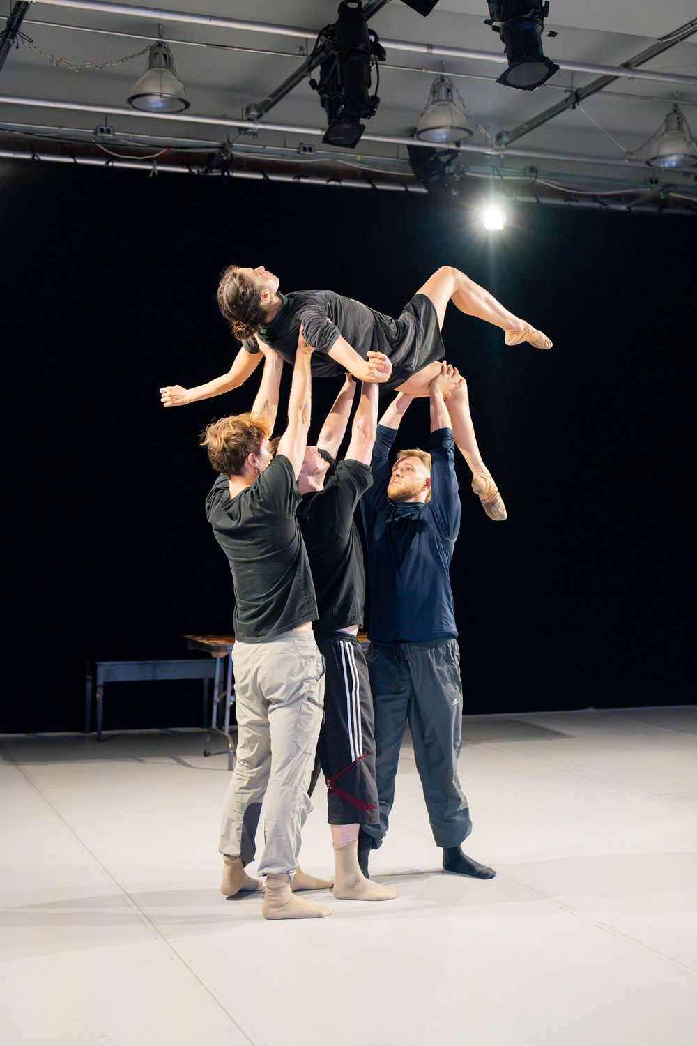Contemporary dancers execute lifts and partnering movements on a white stage floor.