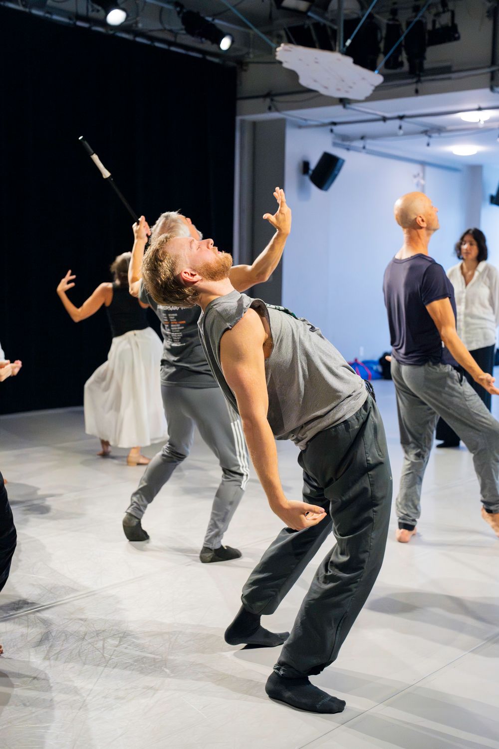 Dancers perform a contemporary dance sequence in a white studio space, demonstrating fluid backward bending movements.