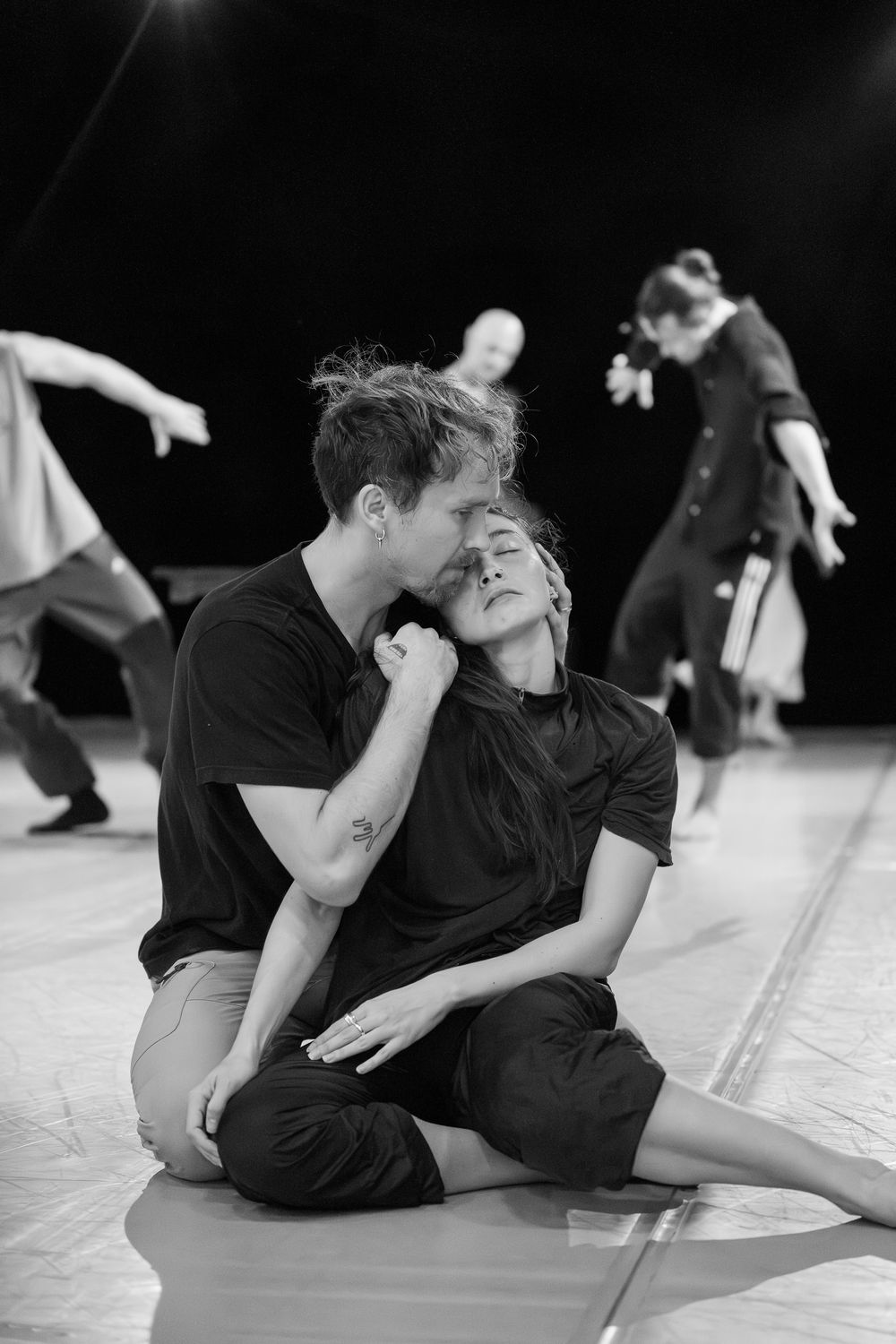 Modern dancers move fluidly across the floor in black attire during a contemporary performance piece.