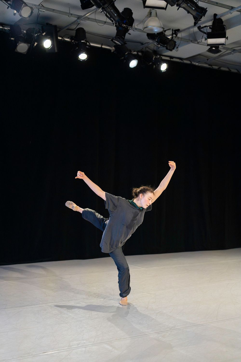 A dancer performs a dynamic sequence of aerial movements on a white stage floor under theatrical lighting.