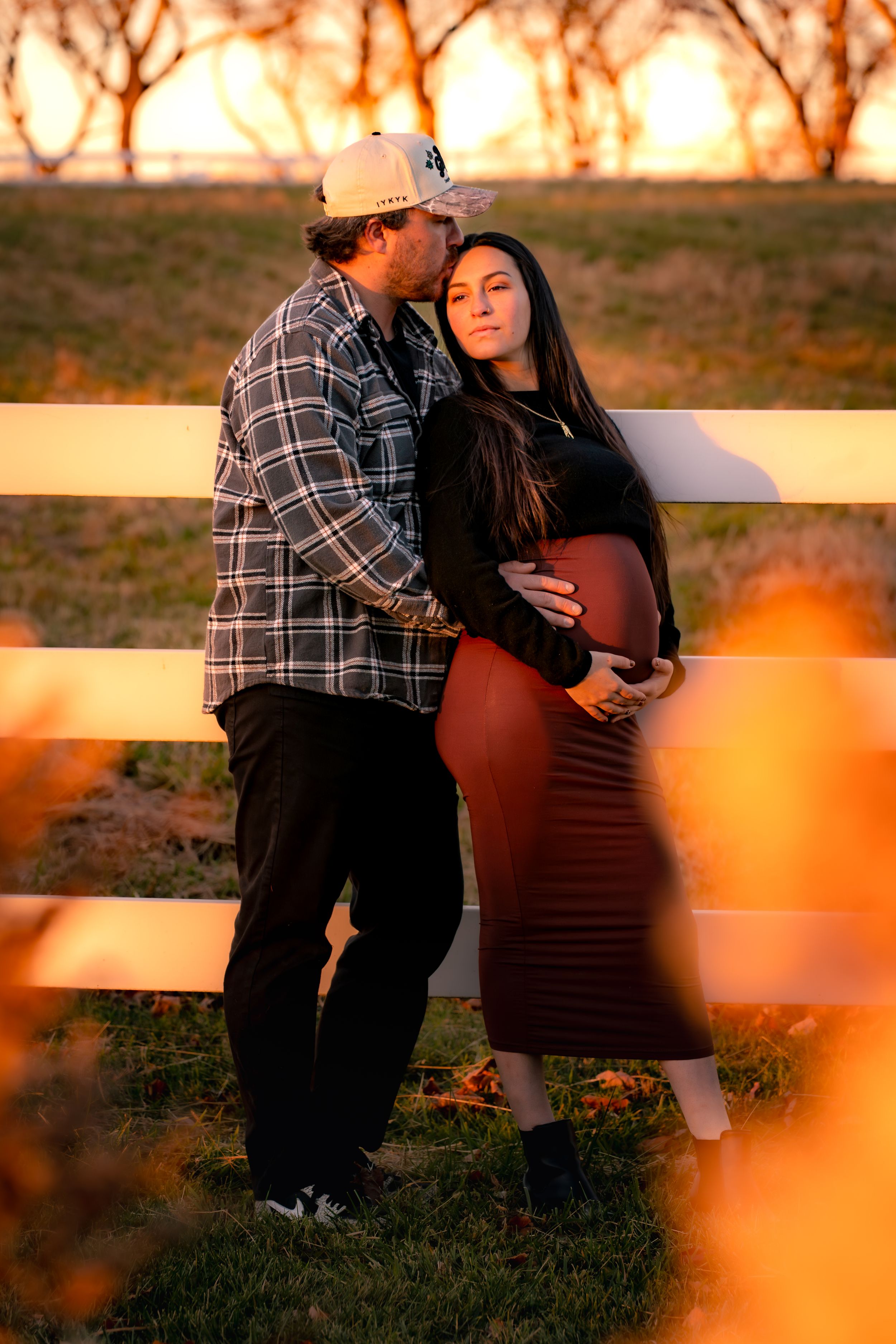 Sunset maternity photoshoot with warm orange tones in an outdoor setting.