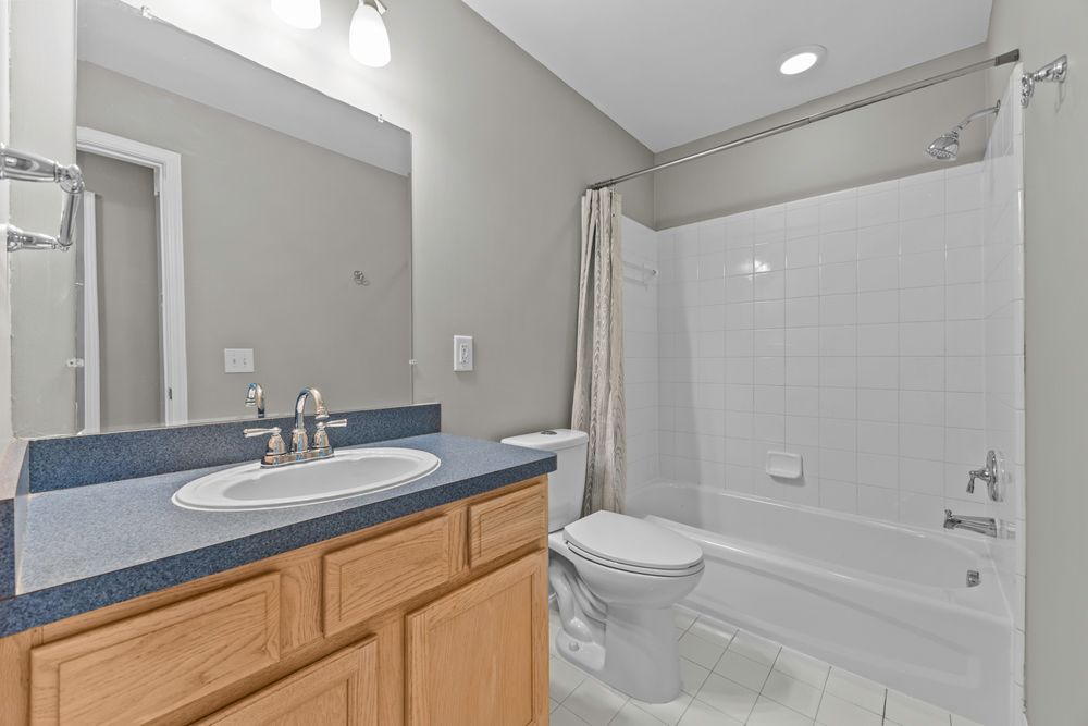 Full bathroom with light wood vanity, blue countertop, white tub-shower combo with tile surround, and toilet.