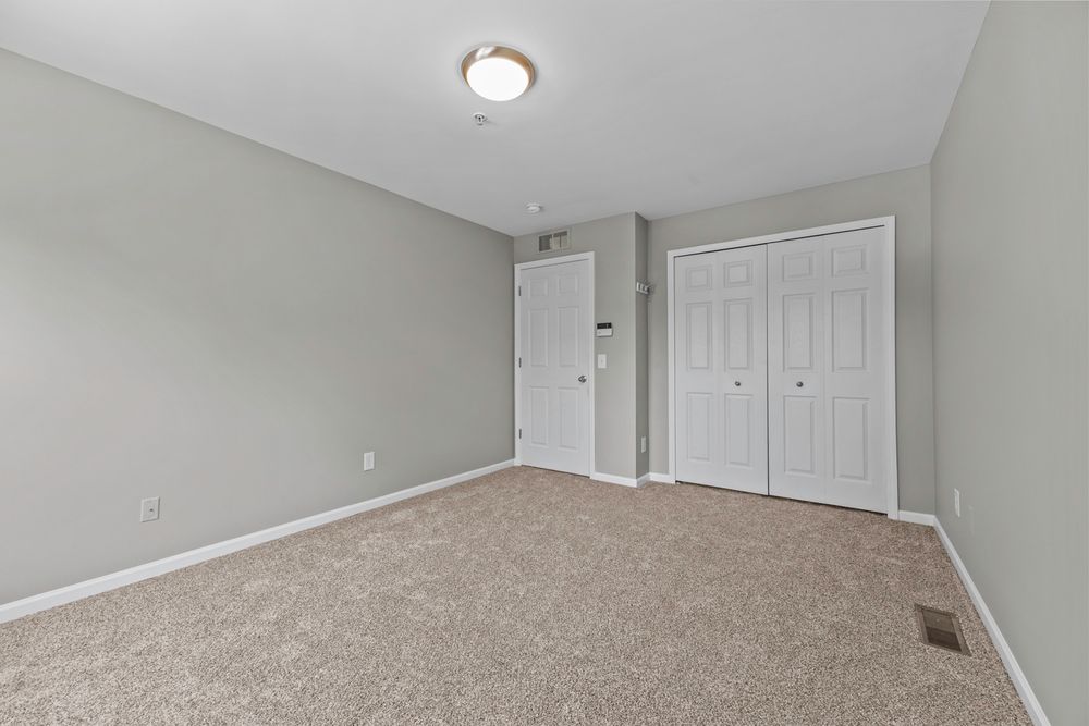 Neutral bedroom with beige carpet, white closet doors, and soft green walls in a clean layout.