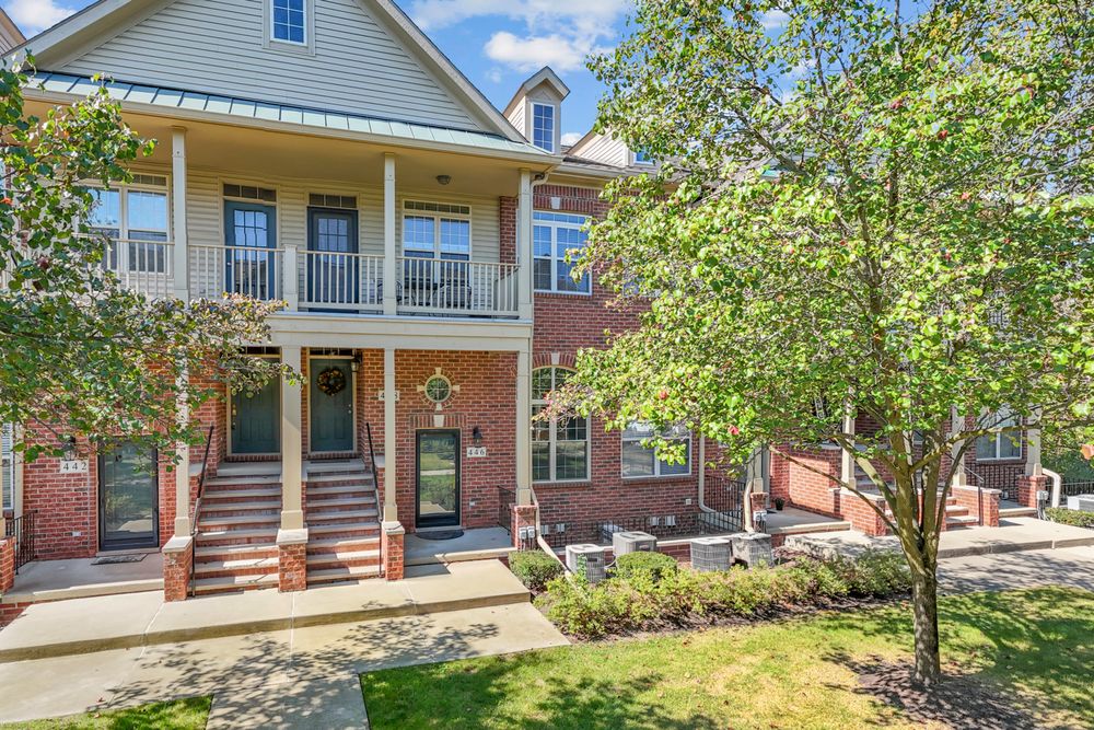 Two-story brick and wood townhomes with covered balconies and young trees in spring.