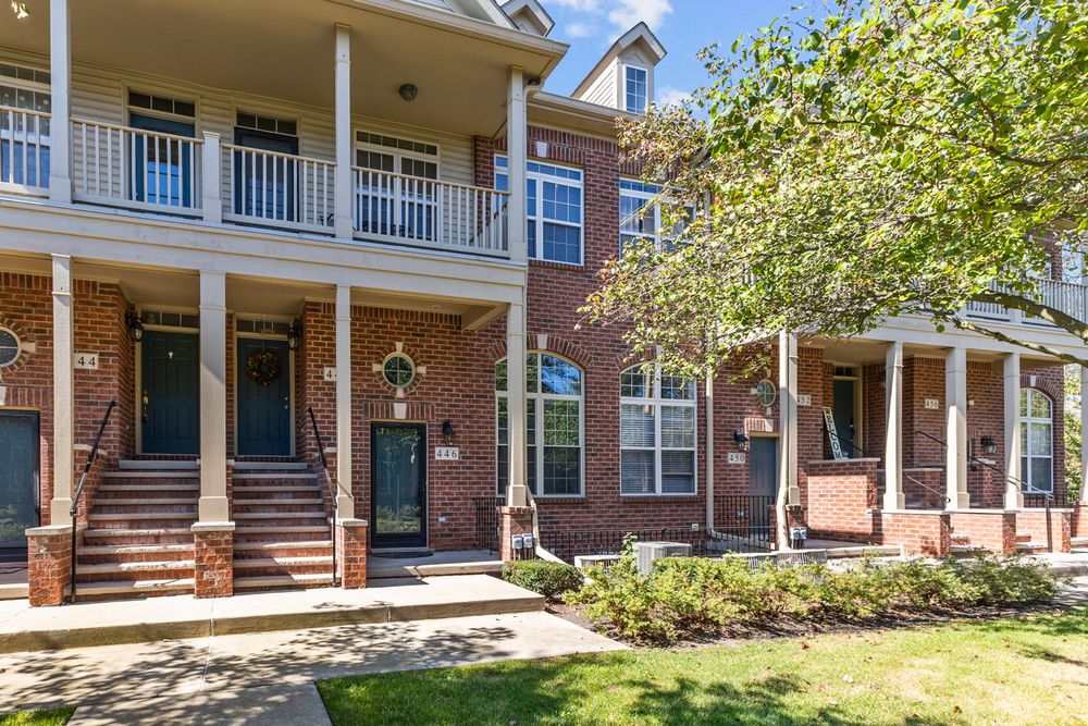 Multi-unit brick townhomes with covered porches and manicured landscaping on sunny day.