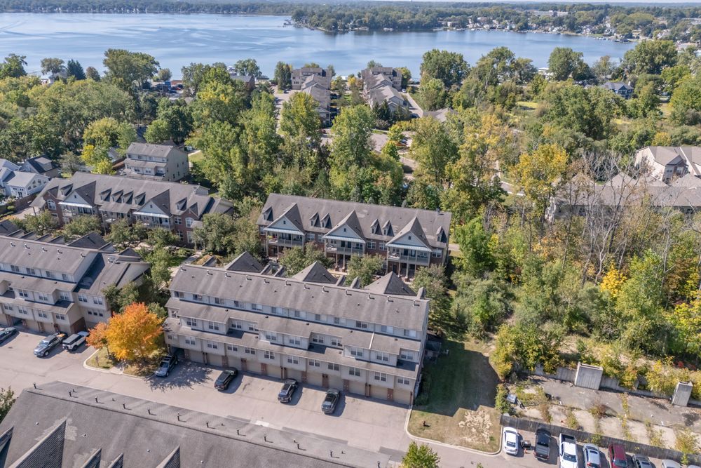 Aerial view of a brick townhome complex surrounded by mature trees with a scenic river visible in the background.