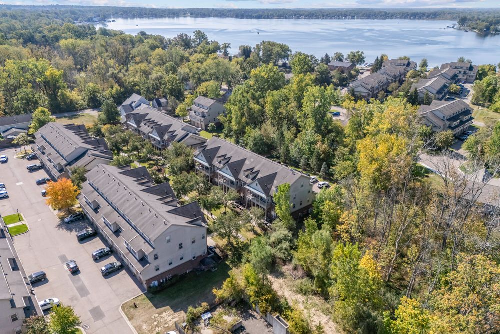 Bird's-eye view of a multi-unit townhome development bordered by lush trees and a serene riverfront setting.