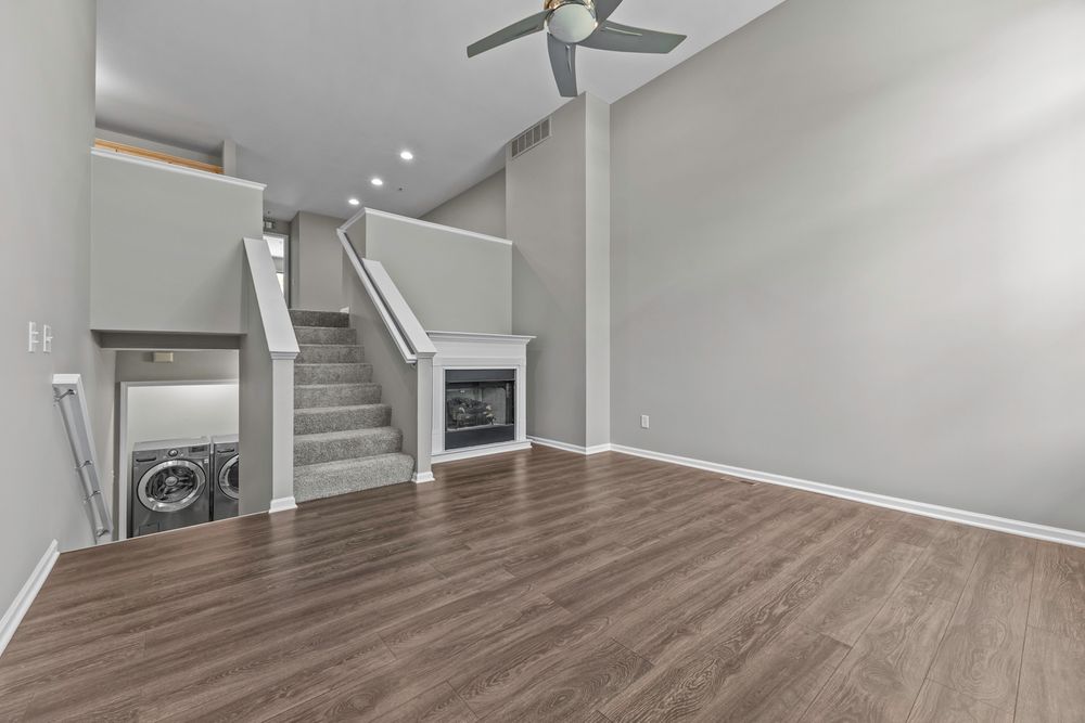 Open living area with hardwood floors, a fireplace, staircase, ceiling fan, and in-unit washer and dryer.