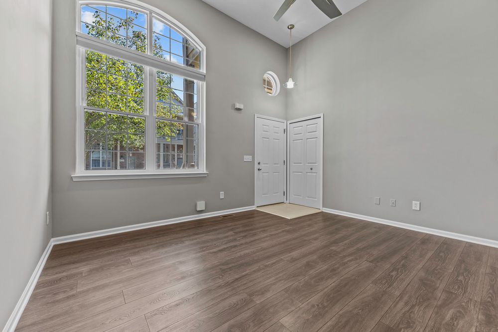 Bright entryway with soaring ceilings, large arched window, hardwood floors, and a ceiling fan in a townhome.