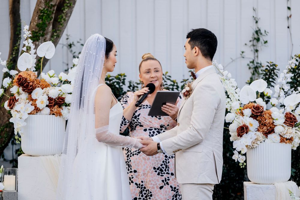 A wedding couple shares intimate moments during their outdoor garden ceremony with white floral arrangements.