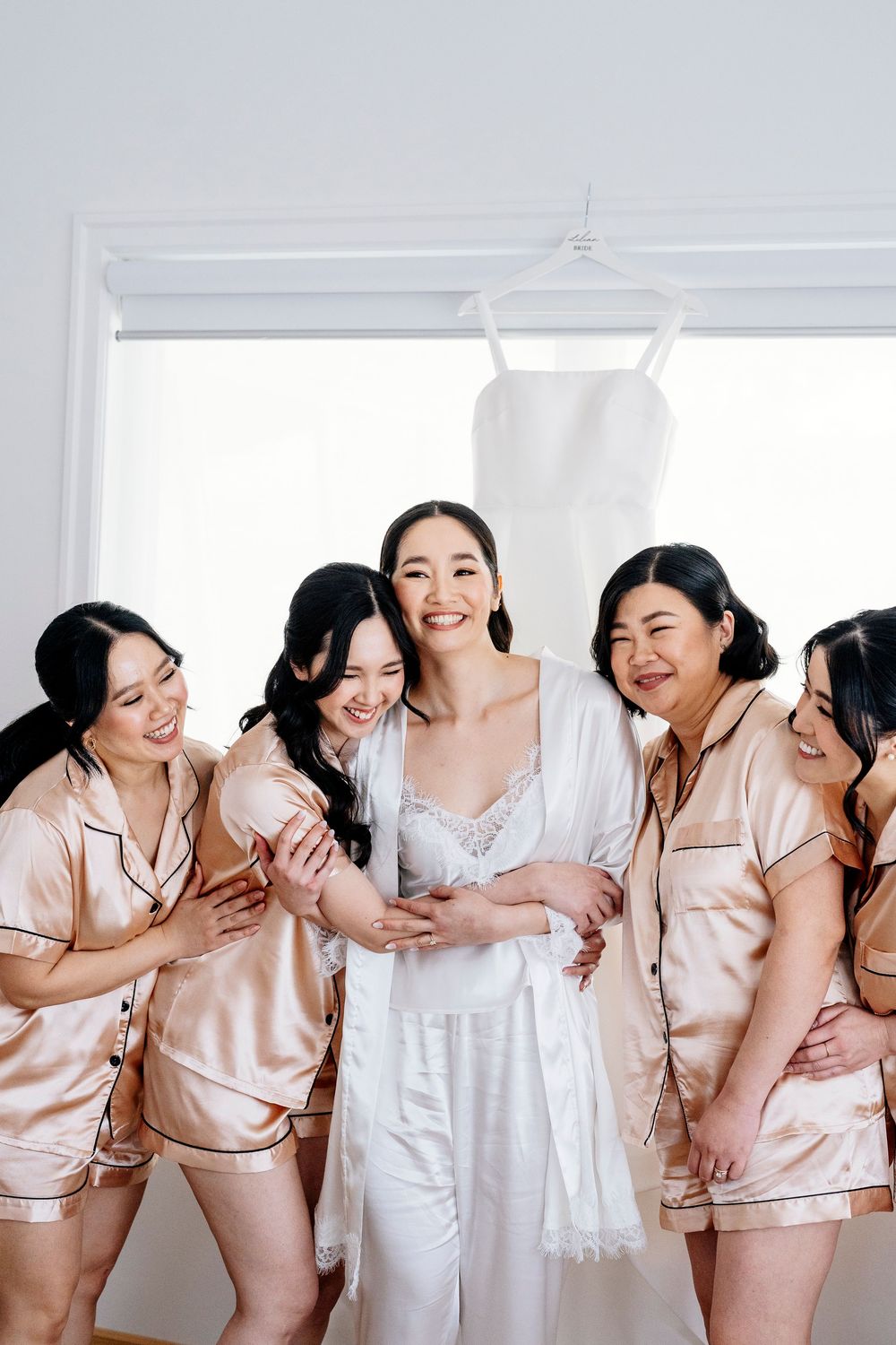 A group wearing matching pink satin pajama sets laughs together in a bright white room.