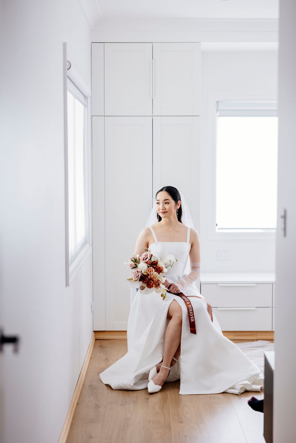 A minimalist bridal portrait series in a bright white room showcases elegant wedding dress details and flowing veil.