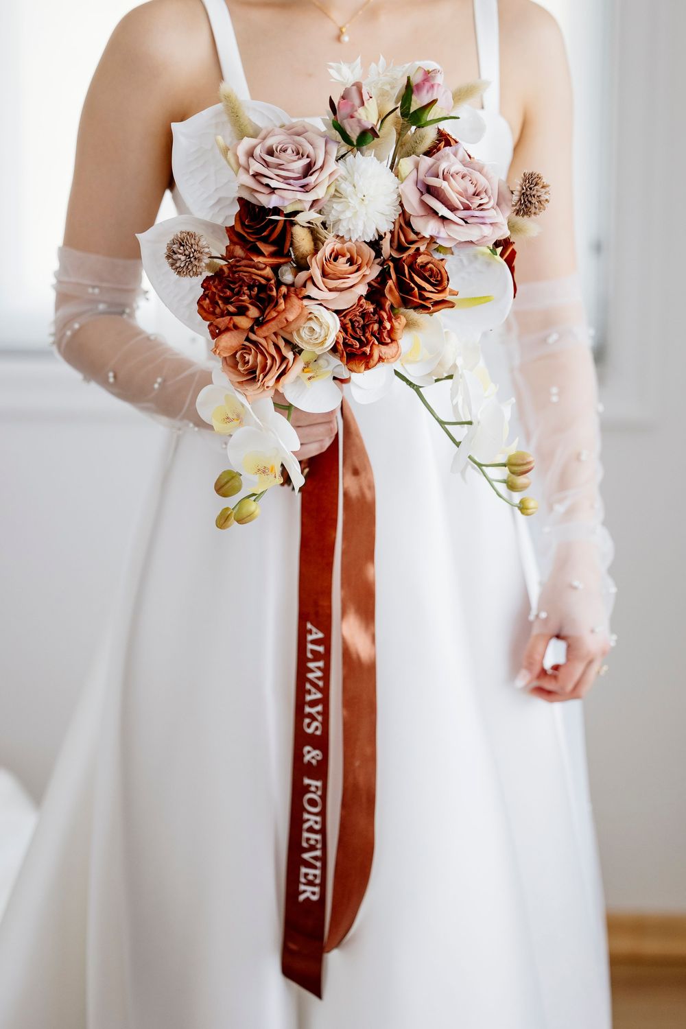 White wedding bouquet with dusty rose and burgundy flowers tied with a velvet ribbon in warm autumn tones.