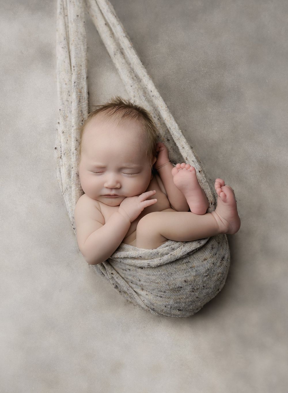 Austin newborn photographer studio portrait of sleeping newborn posed in soft fabric sling on neutral backdrop