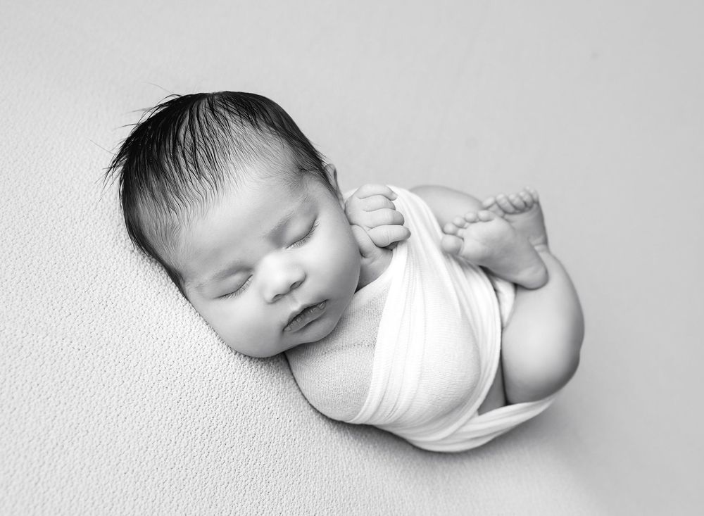 Black and white newborn portrait by Austin newborn photographer featuring baby wrapped and posed on studio backdrop