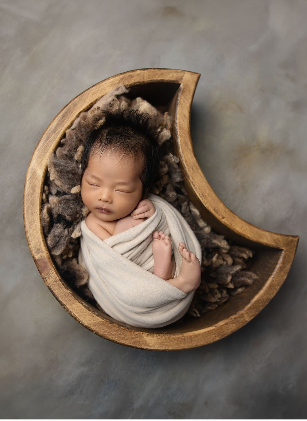 Artistic newborn photography in Austin featuring baby wrapped and posed in wooden moon prop