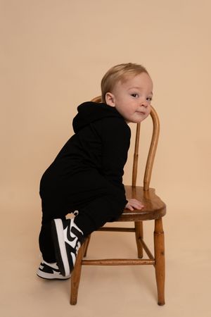 Small child in black outfit exploring a wooden chair against beige background in progressive action shots.