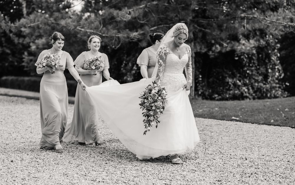 Wedding party walks together in a line across a scenic outdoor garden path during a summer celebration. Relaxed Dorset Wedding photographer
