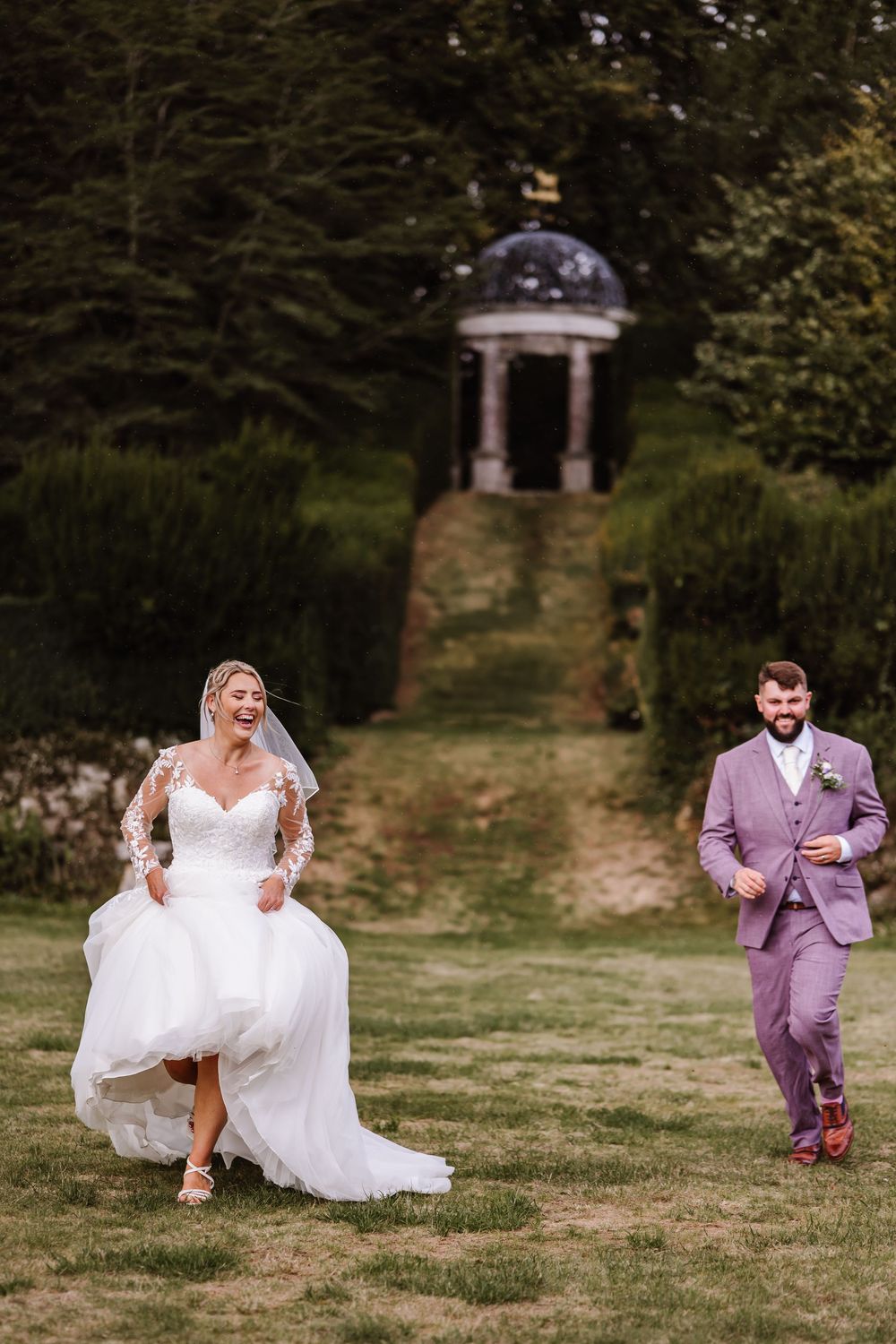 Wedding couple playfully runs and dances across a grassy lawn on their special day, showing joy and celebration. Relaxed Dorset Wedding phot