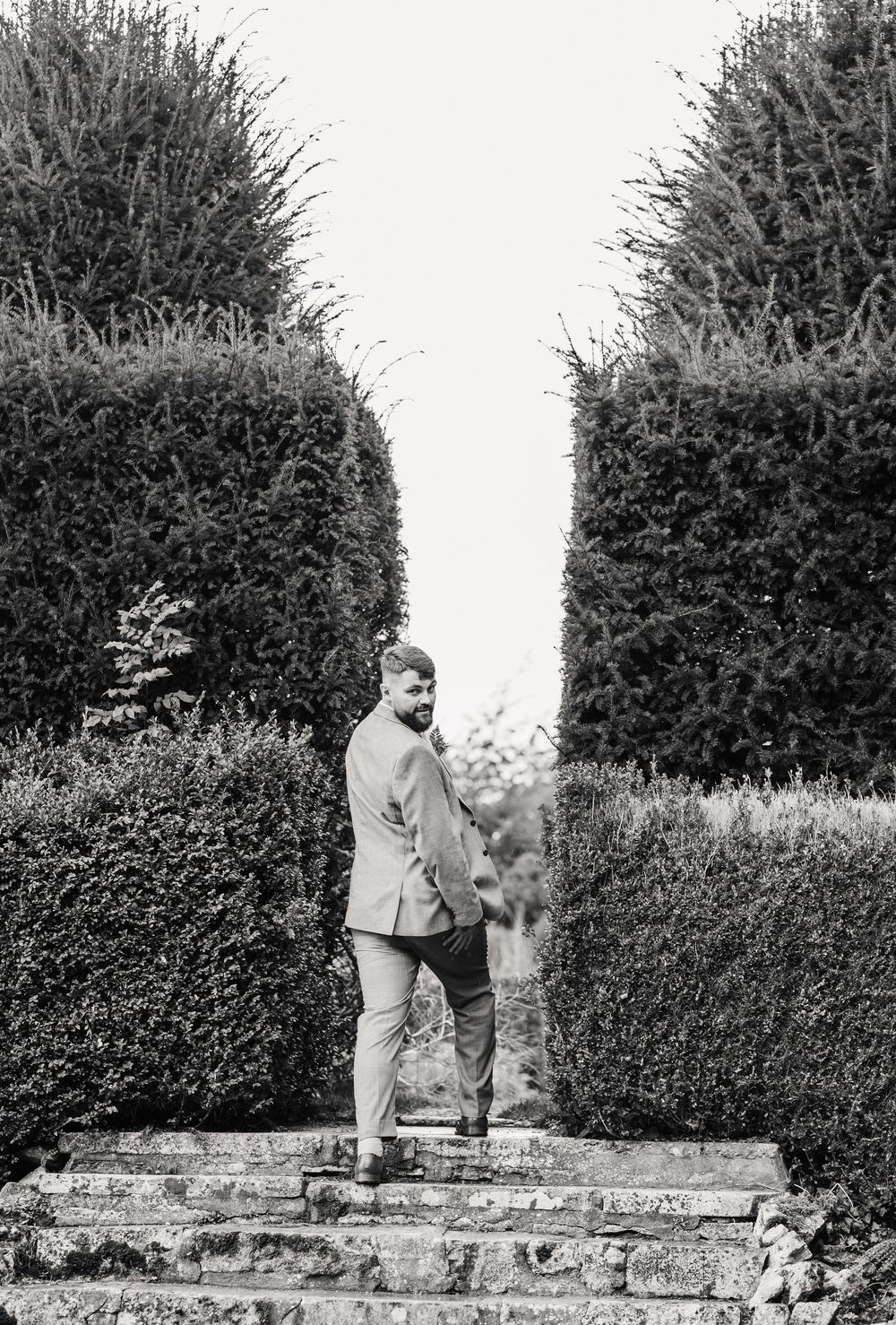 A sequence of black and white photographs showing someone walking along a stone wall in a garden with hedges. Relaxed Dorset Wedding photo