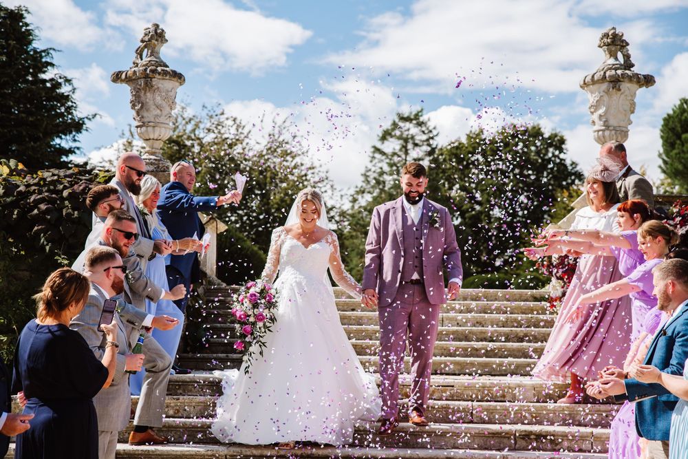 Confetti fills the air on grand stone steps during an outdoor celebration with guests in colorful attire. Relaxed Dorset Wedding photographe