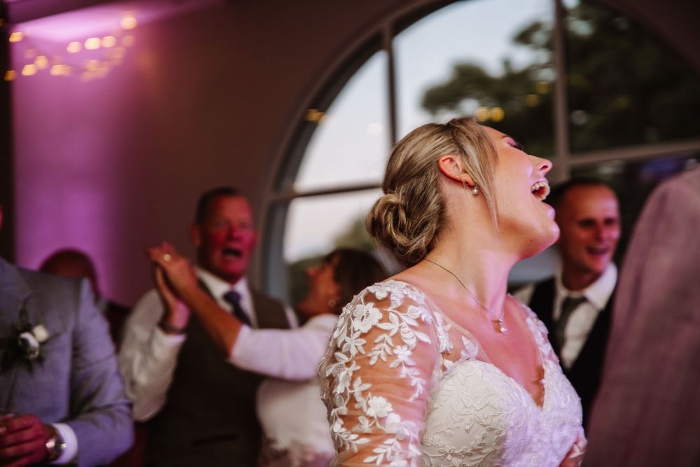 A group of wedding guests dancing and celebrating on the dance floor with purple lighting in the background. Relaxed Dorset Wedding photo