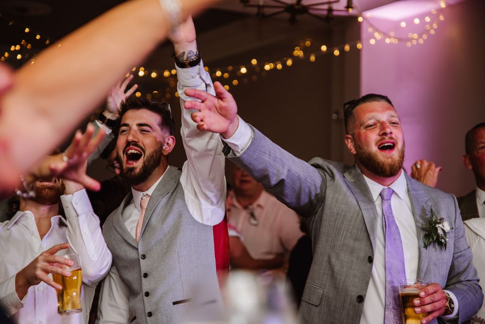 A group of wedding guests raise their glasses and cheer during a celebratory toast at a reception with pink lighting. Relaxed Dorset Wedding
