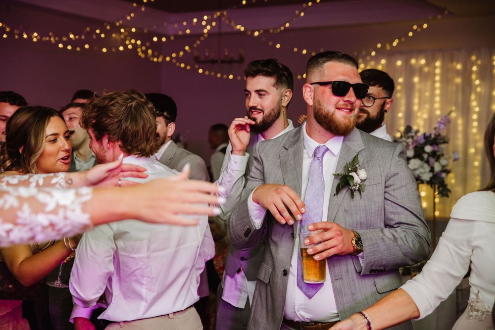 Wedding guests dancing and celebrating at a reception with twinkle lights and festive atmosphere in the background. Relaxed Dorset Wedding