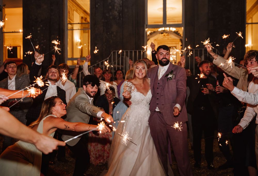Wedding guests hold sparklers in a nighttime sendoff celebration creating a magical glowing archway for the newlyweds.