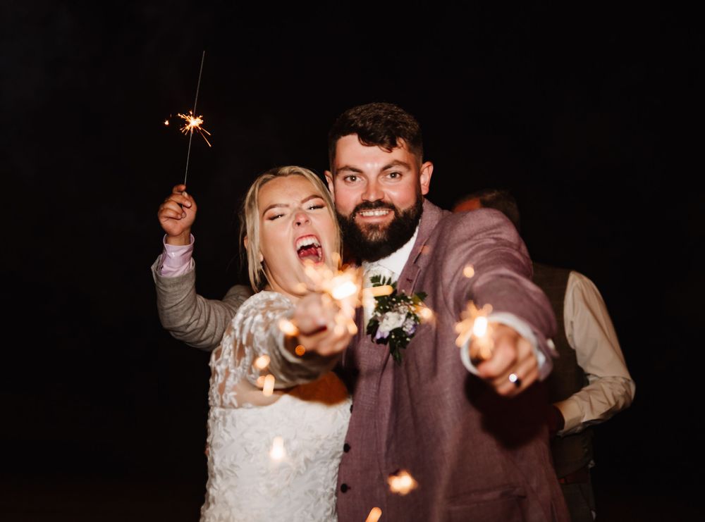 A couple celebrates at their wedding reception while holding sparklers and dancing in a dark setting. Relaxed Dorset Wedding photographer