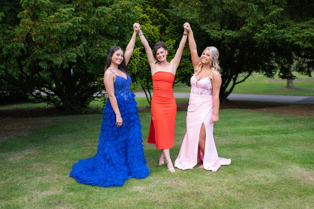 Group posing in colorful formal attire on a lush green lawn during a special event.