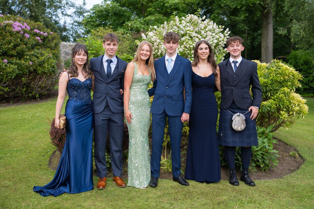 Formal group photo with attendees in navy suits and dresses against garden backdrop.