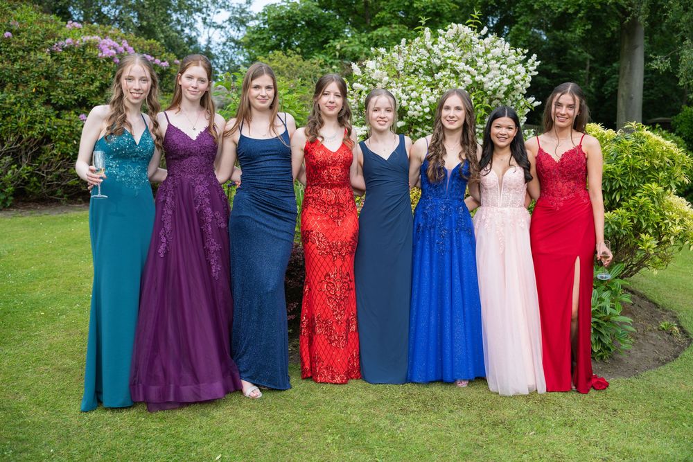 Celebration group wearing mix of formal dresses in vibrant colors posed outdoors.