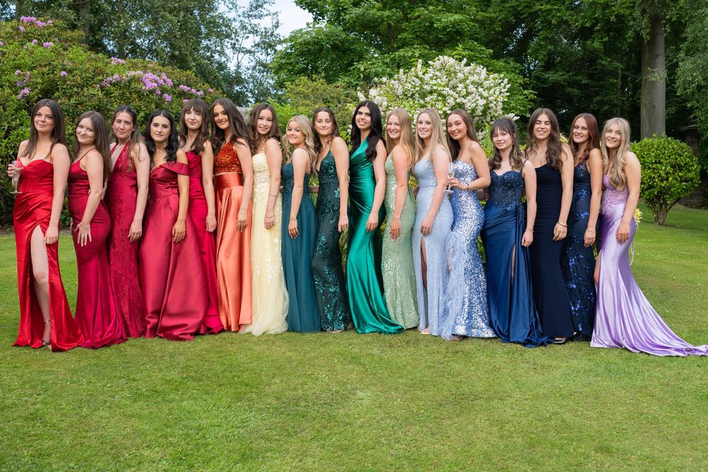 Large formal gathering with attendees in rainbow of elegant dresses on garden lawn.