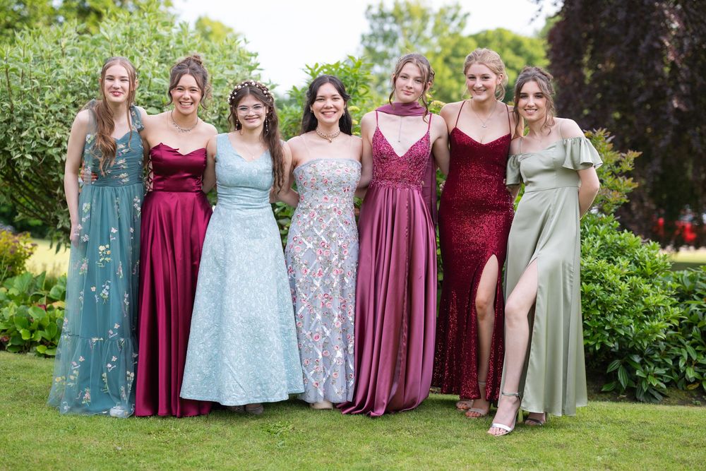 Group photo featuring mix of pastel and burgundy formal dresses in garden setting.