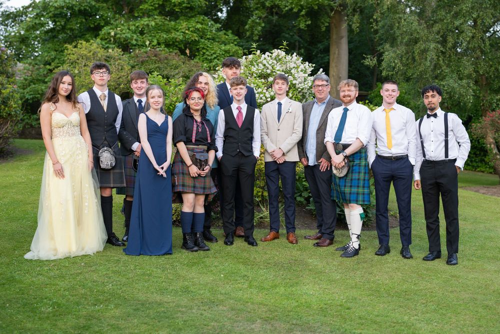 Event attendees in formal attire gathered for group photo on sunny garden grounds.