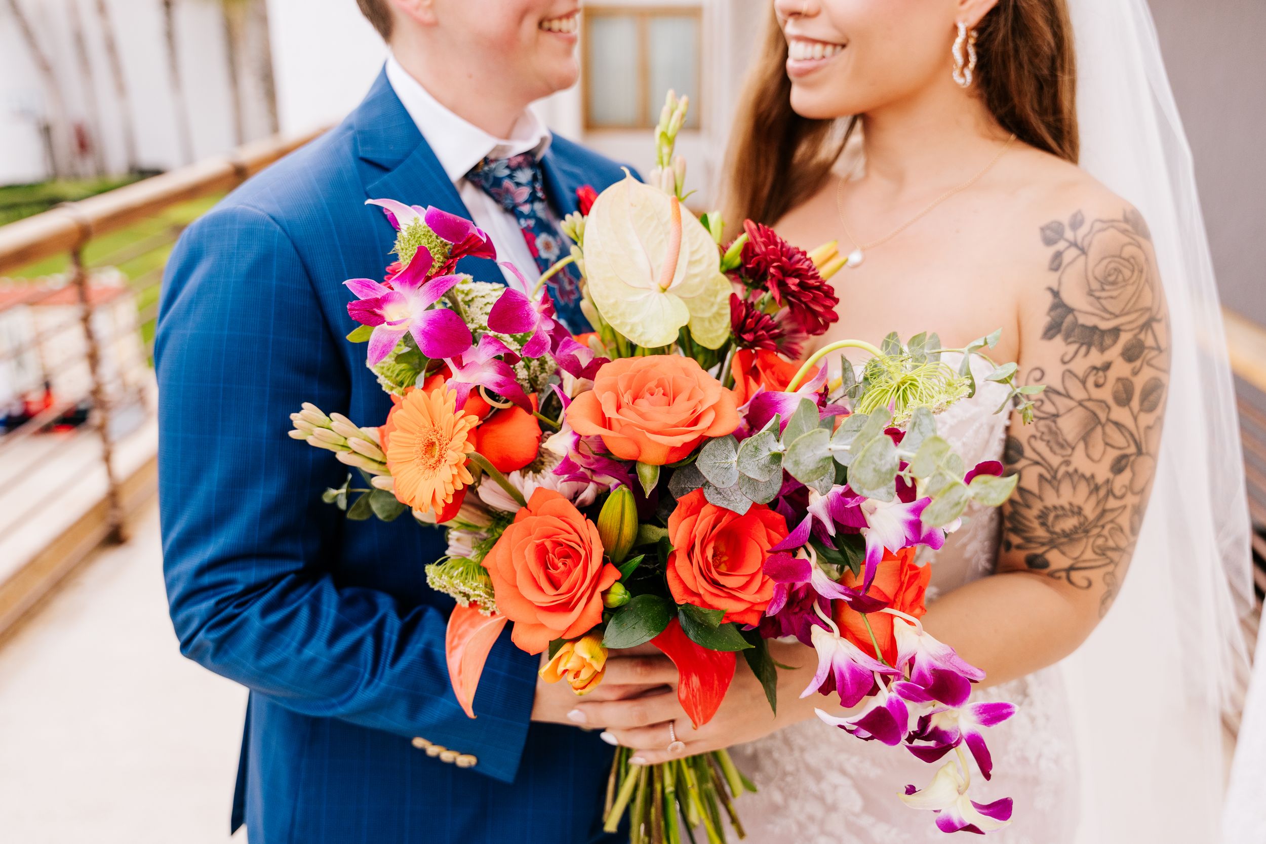 Bride and groom holding vibrant orange, pink, and purple wedding bouquet with roses and orchids on their wedding day.