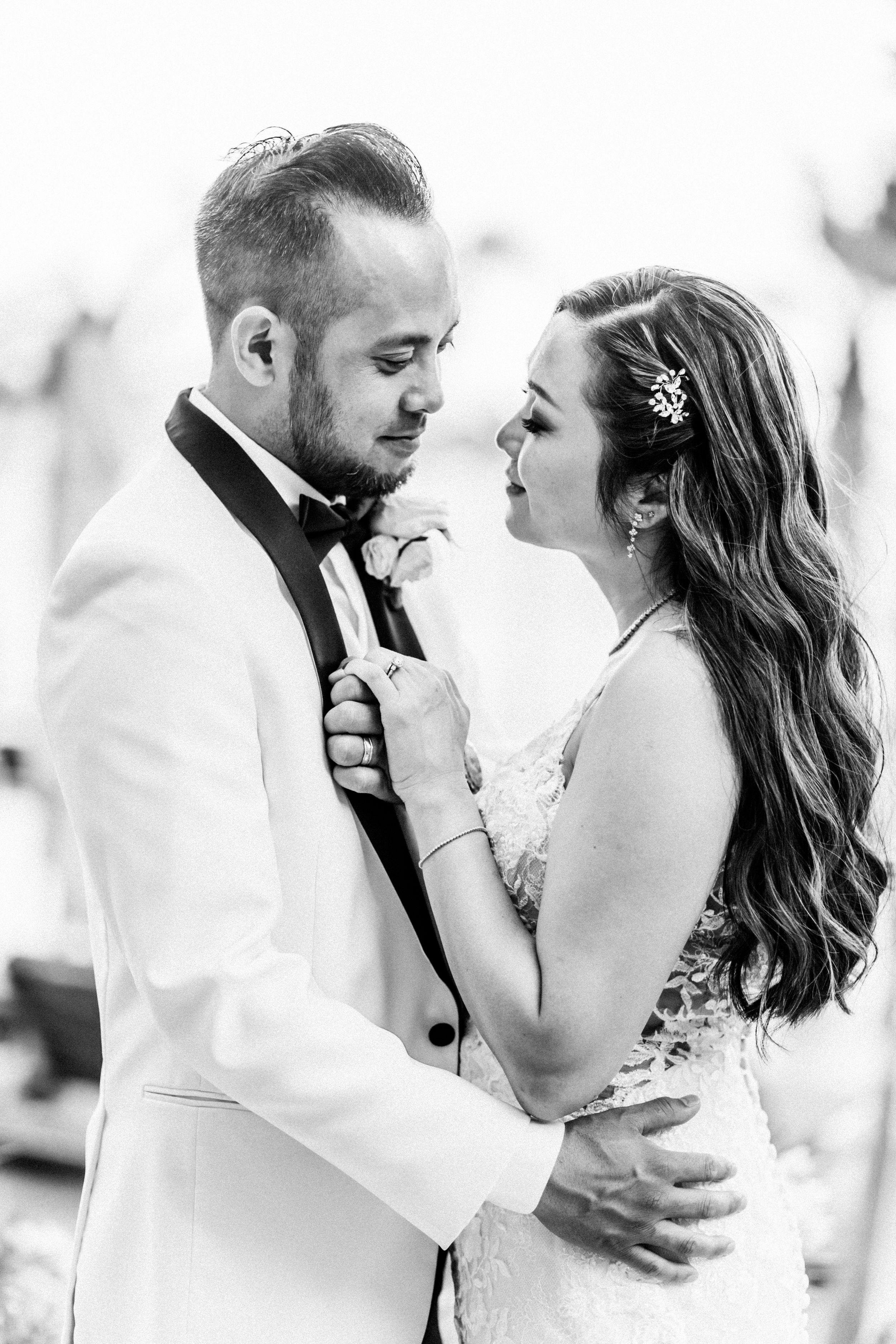 Black and white photo of a bride and groom embracing, sharing an intimate moment in wedding attire.