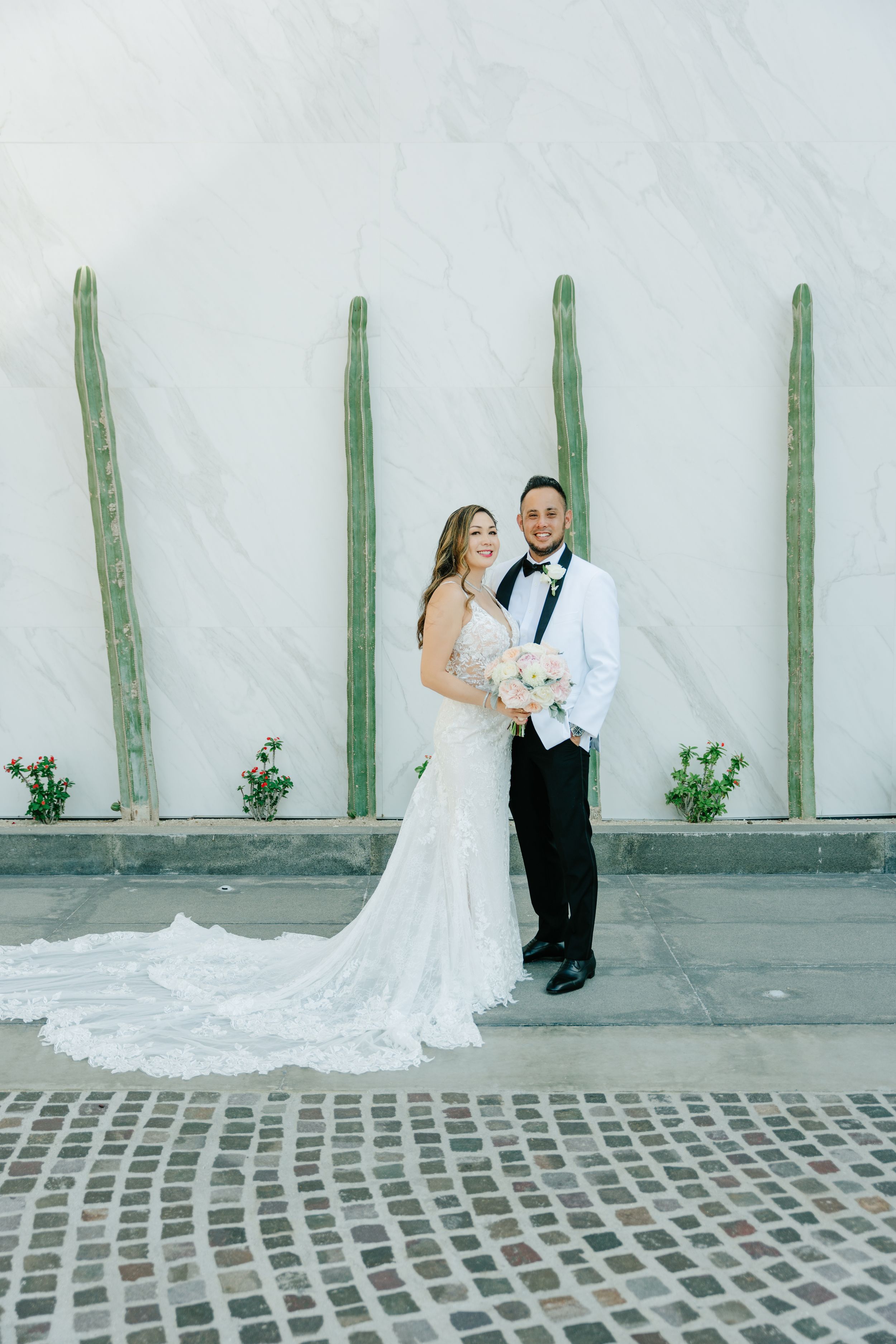 A romantic wedding photo series showing a couple posing against a gray wall with green cacti in an urban setting.